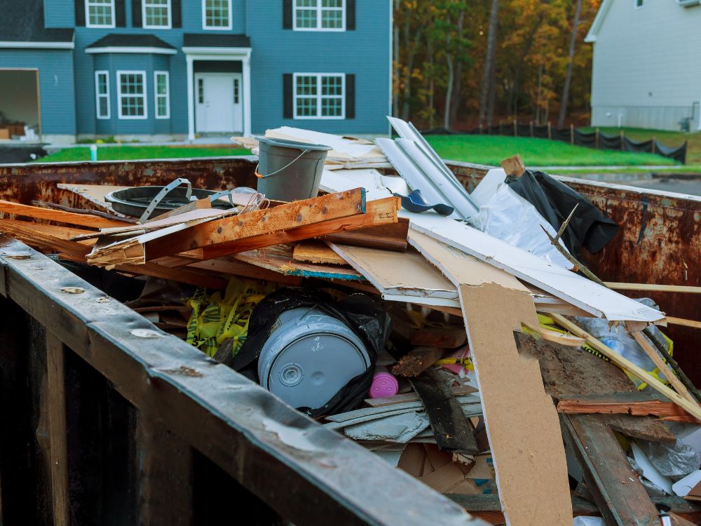 A dumpster overflowing with debris sits in front of a house